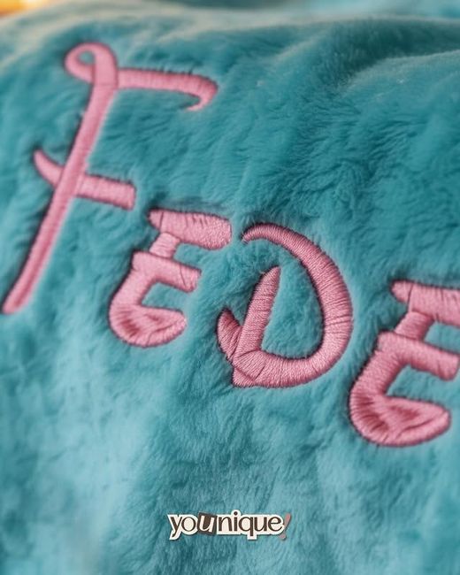 Tessuto felpato turchese con lettere rosa ricamate che compongono la scritta 