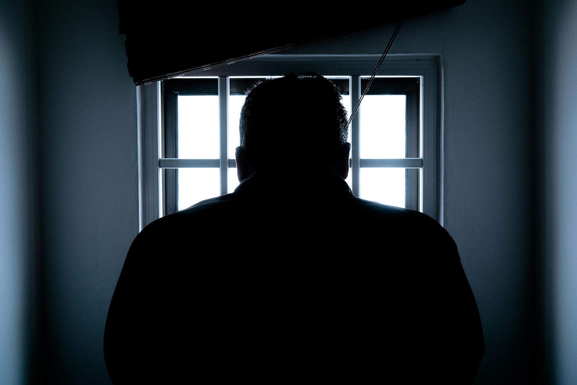 A man is standing in front of a window in a dark room.