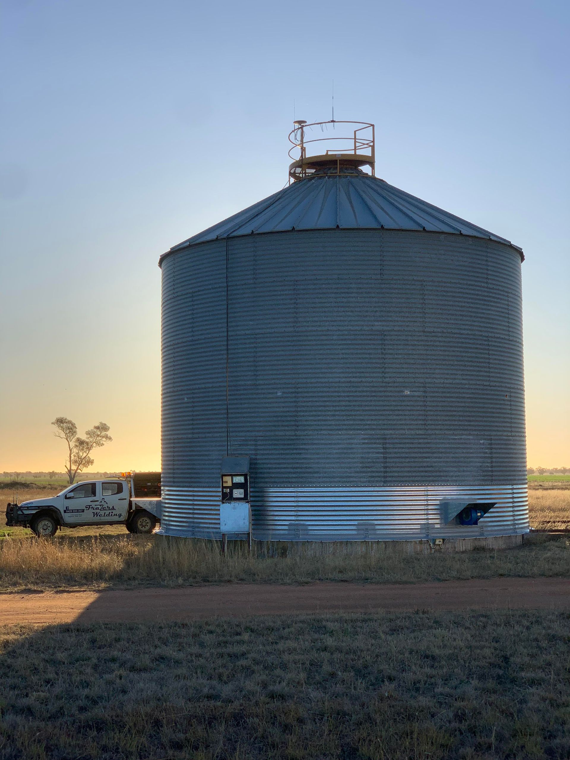 A Large Silo in a Field With a Truck Parked in Front of It — Welders In Gilgandra, NSW