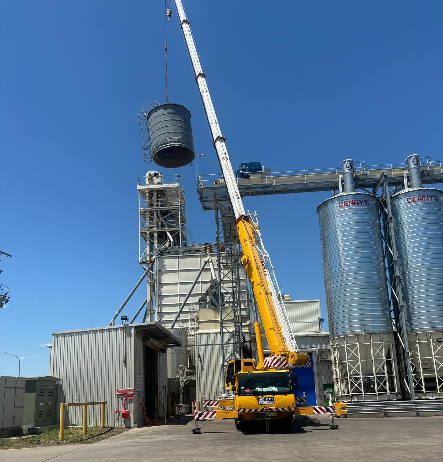 A Large Yellow Crane is Lifting a Large Cylindrical Object — Welders In Gilgandra, NSW