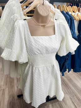 A white dress is hanging on a mannequin in a store.
