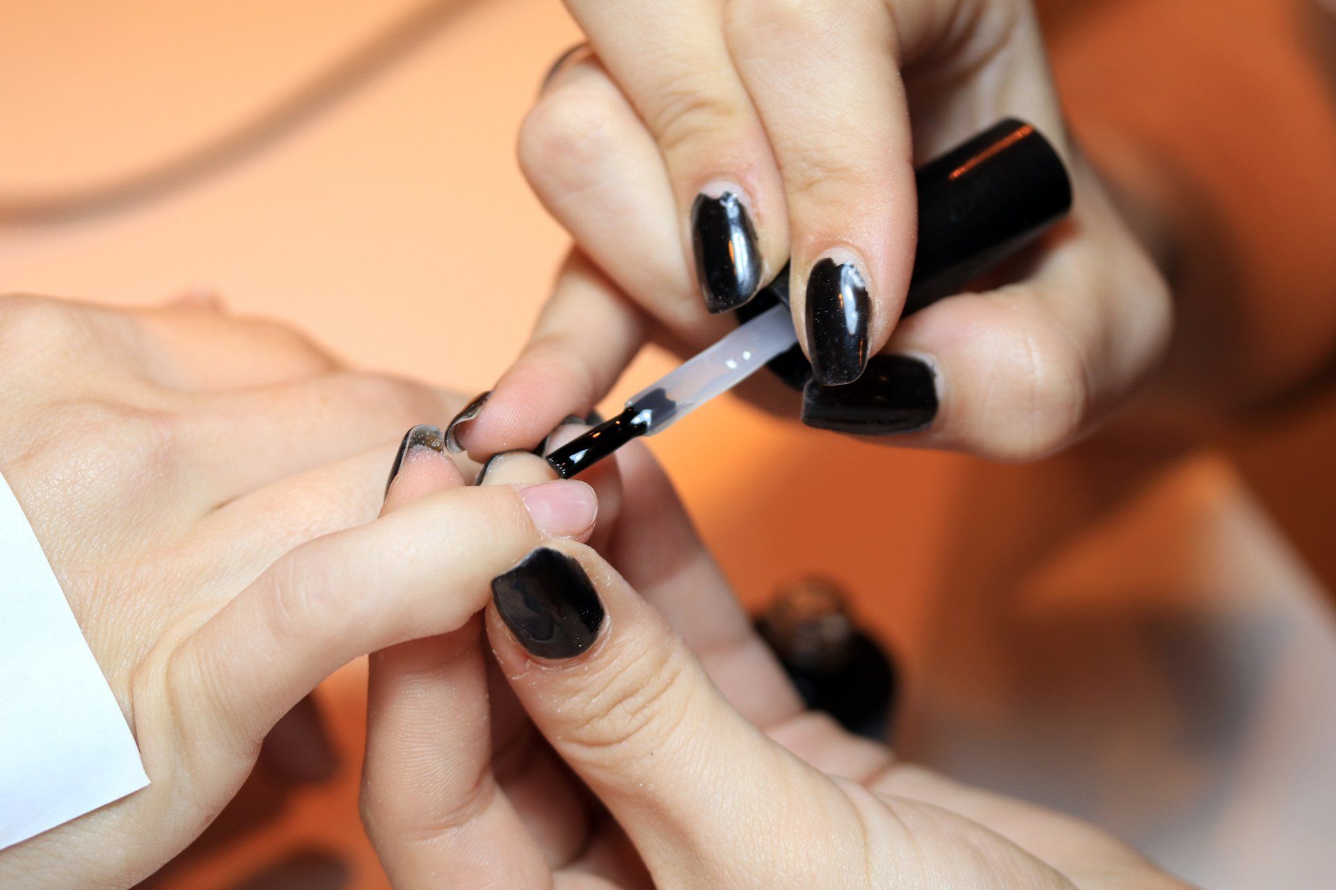 Una persona está aplicando esmalte de uñas negro en las uñas de otra persona.