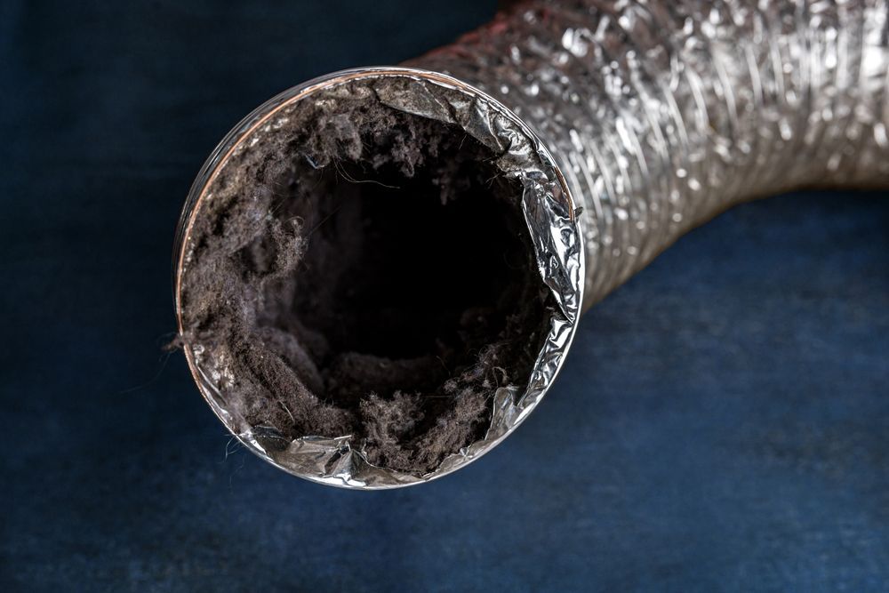 Close-up of a clogged silver flexible hose with dark debris inside on a blue background