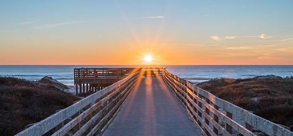 A wooden pier leading to the ocean at sunset.