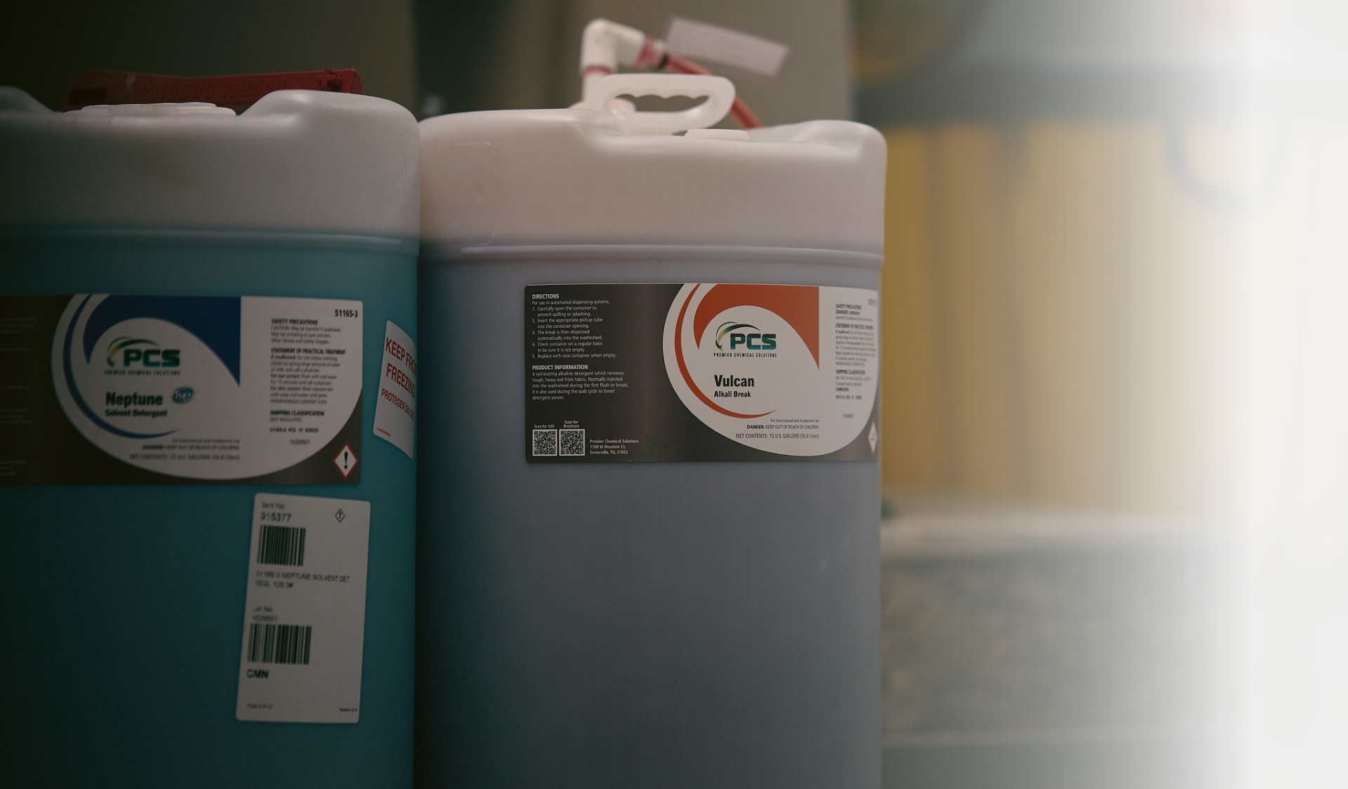 Two large industrial containers, one teal and one grey, with PCB labels, possibly containing chemicals.