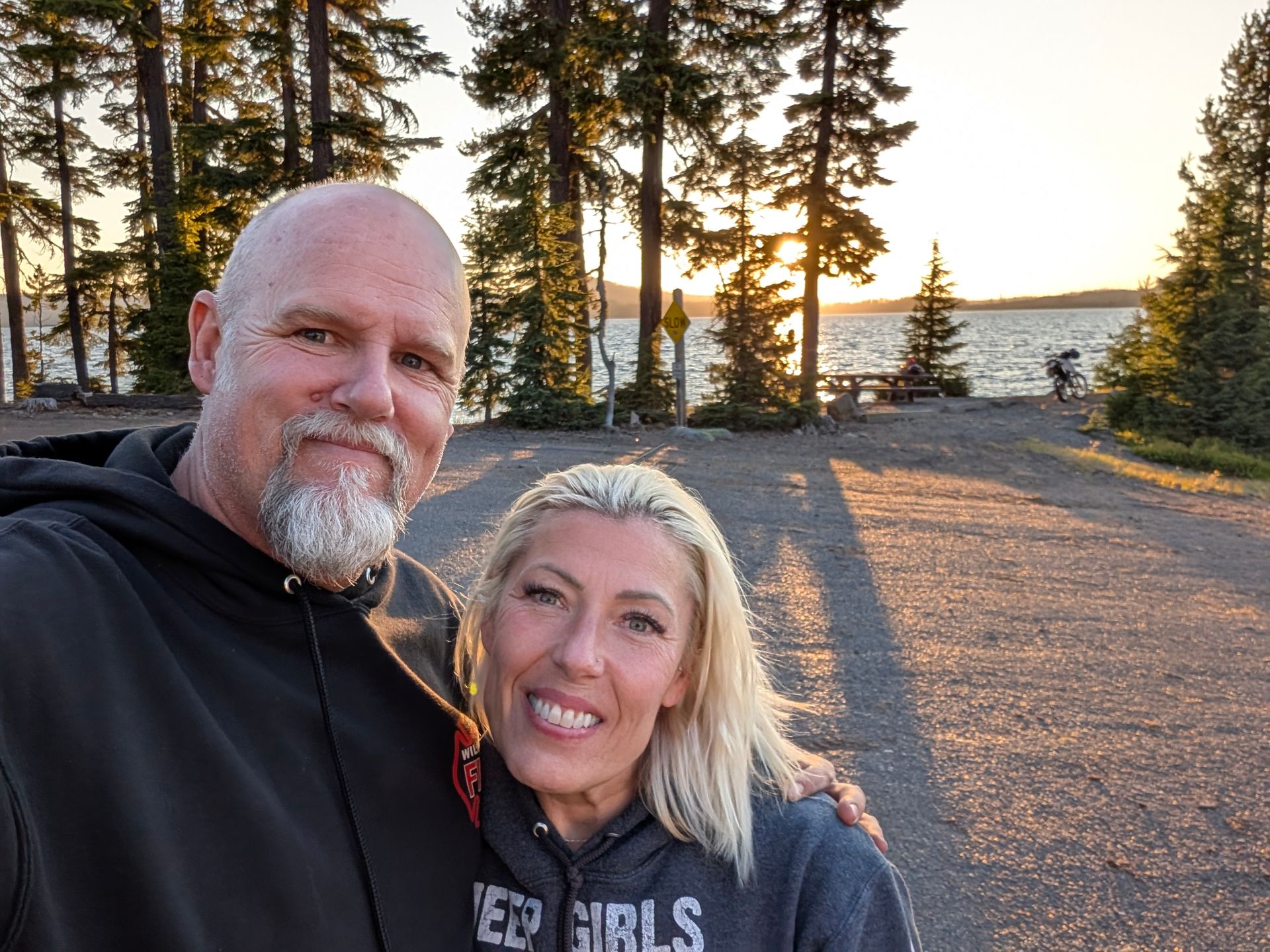 A man and a woman are posing for a picture in front of a lake.