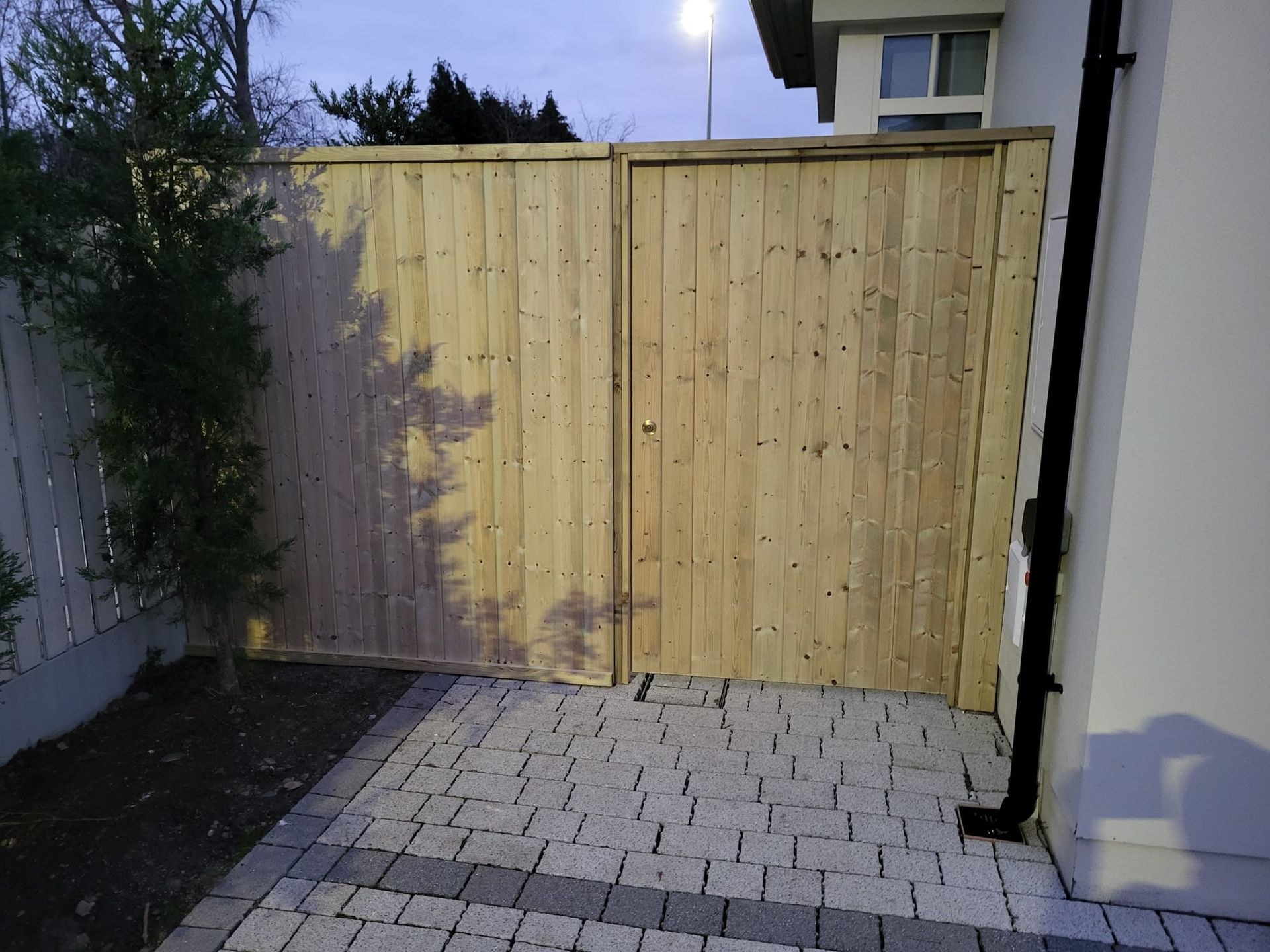 A wooden fence surrounds a brick walkway in front of a house