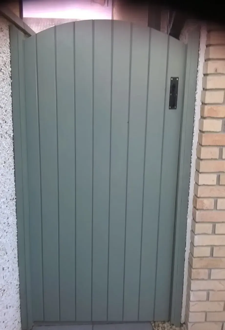 A green wooden gate is sitting next to a brick wall.