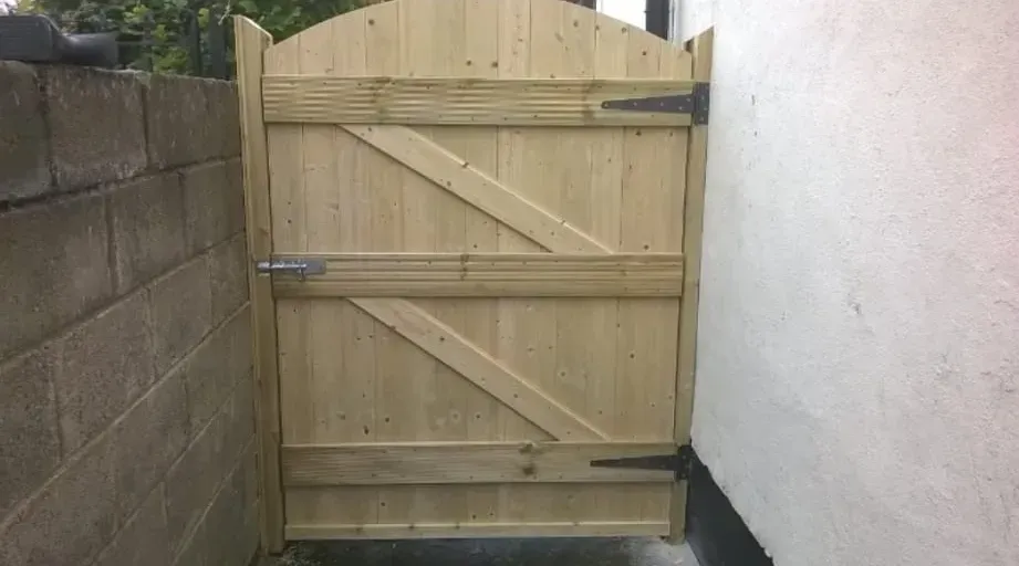 A wooden gate is sitting next to a brick wall.