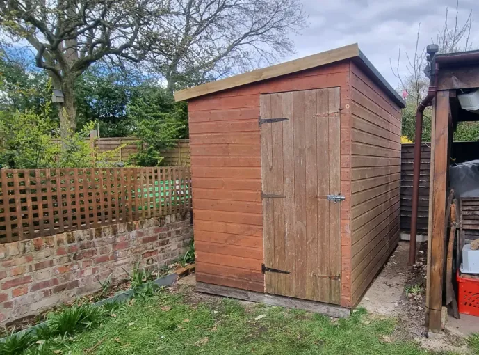 A small wooden shed in a backyard next to a brick wall.