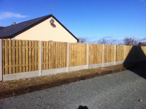A wooden fence surrounds a gravel driveway in front of a house.