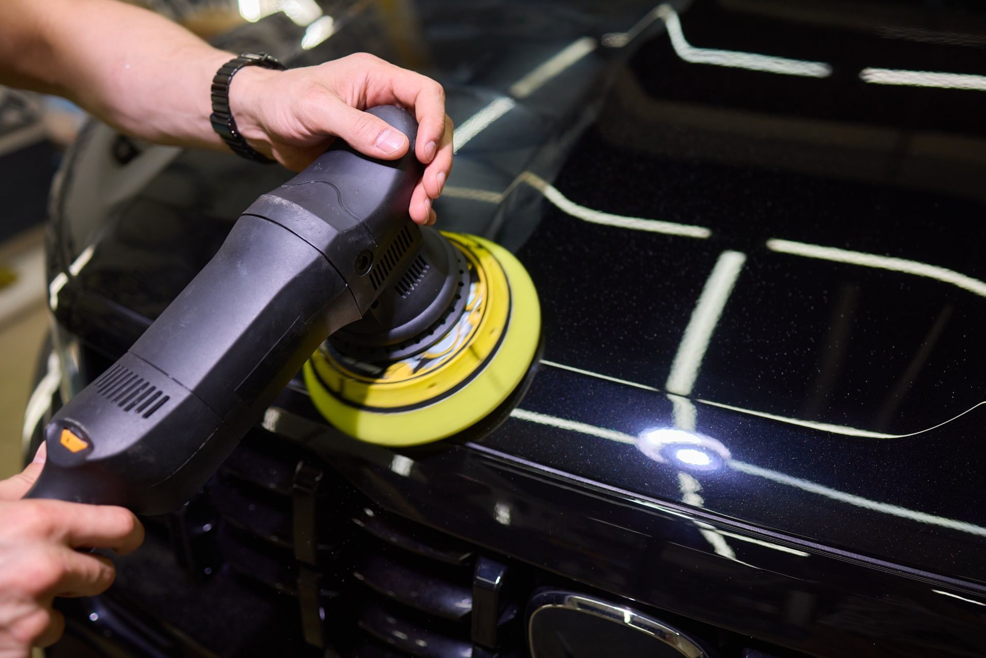 A man is polishing a black car with a machine.