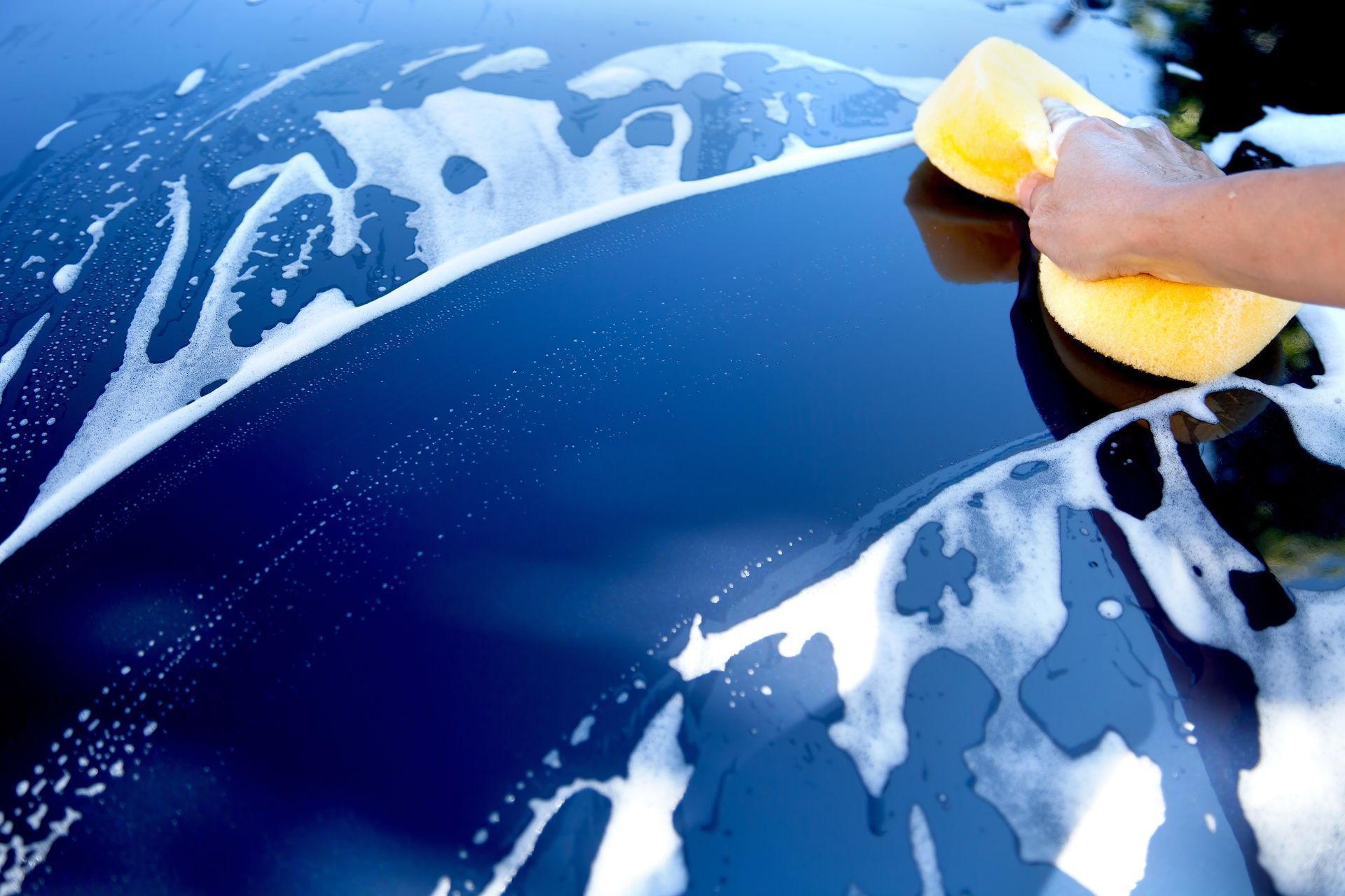 A person is washing a car with a yellow sponge.