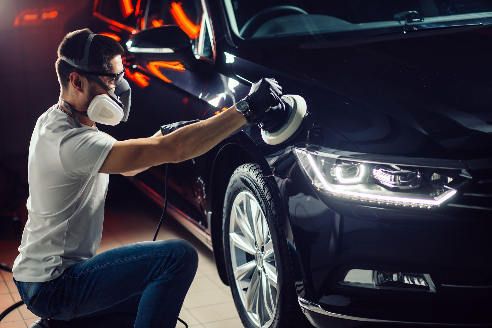 A man wearing a mask is polishing a black car.