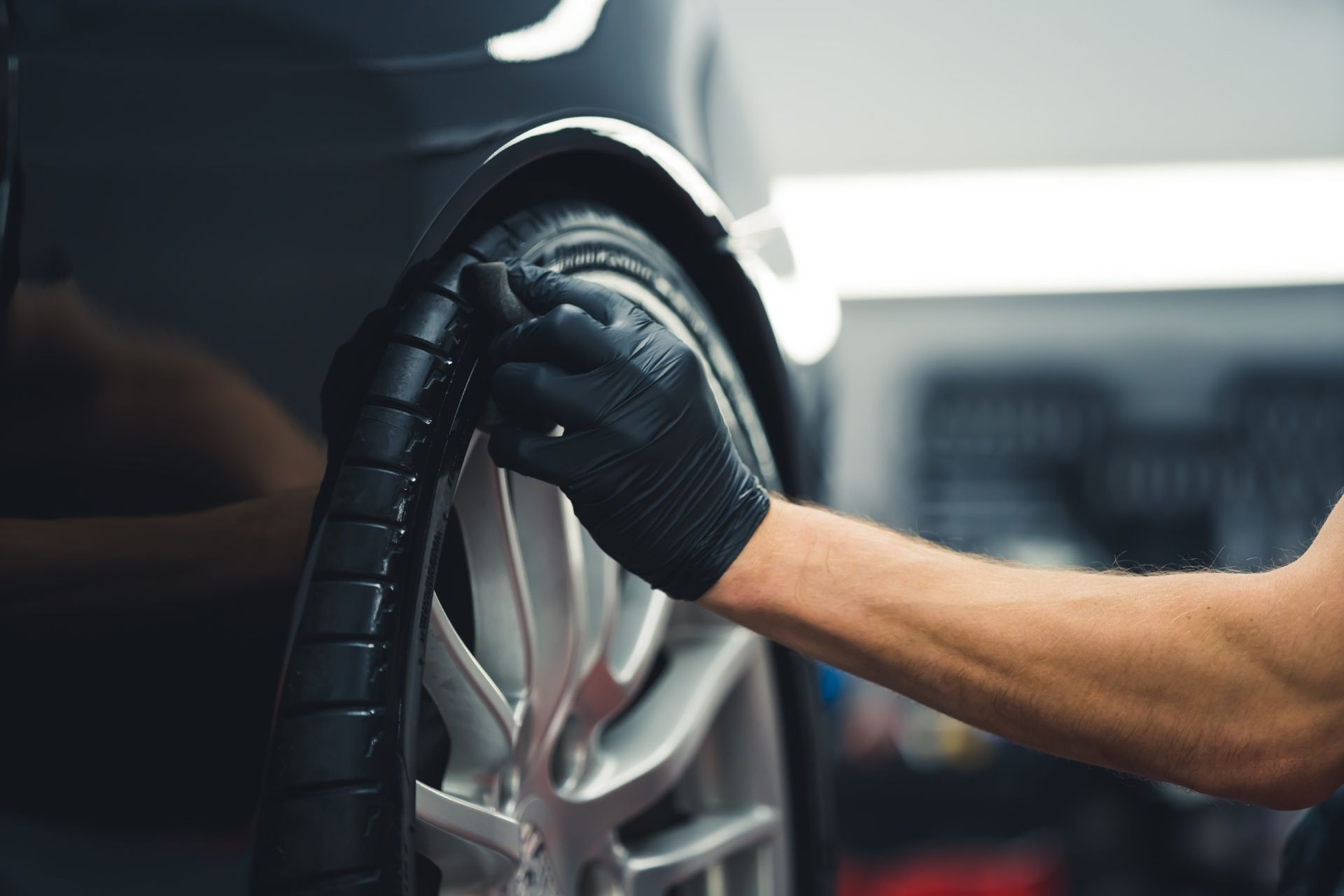 A man wearing black gloves is changing a tire on a car.