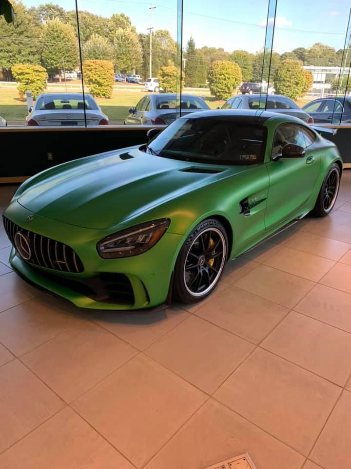 A green mercedes amg gt r is parked in a showroom.