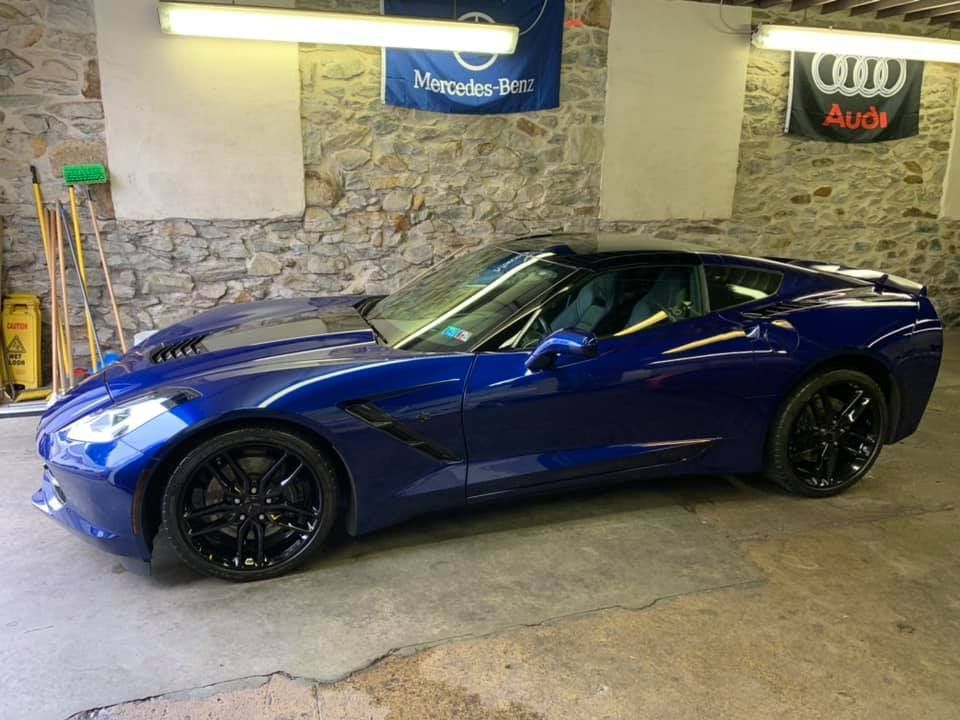 A blue sports car is parked in a garage next to a mercedes benz and audi flag.