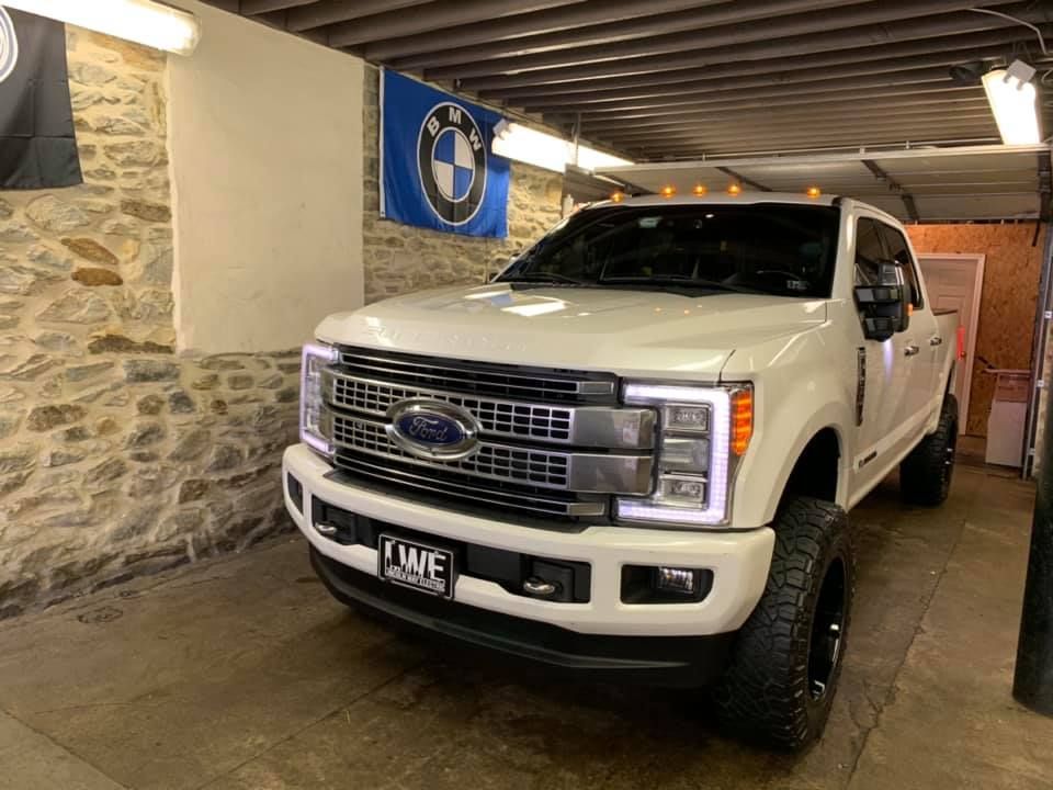 A white ford truck is parked in a garage next to a bmw flag.