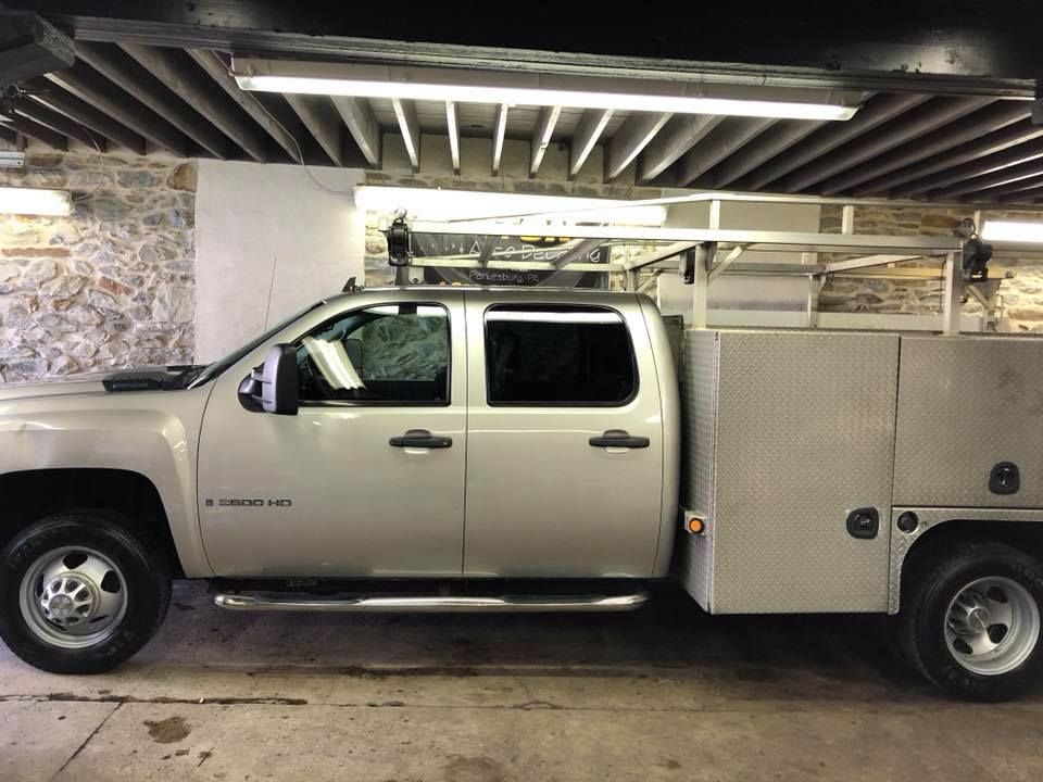 A silver truck with a ladder rack on top of it is parked in a garage.