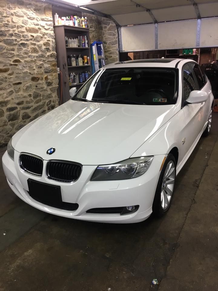A white bmw is parked in a garage next to a stone wall.