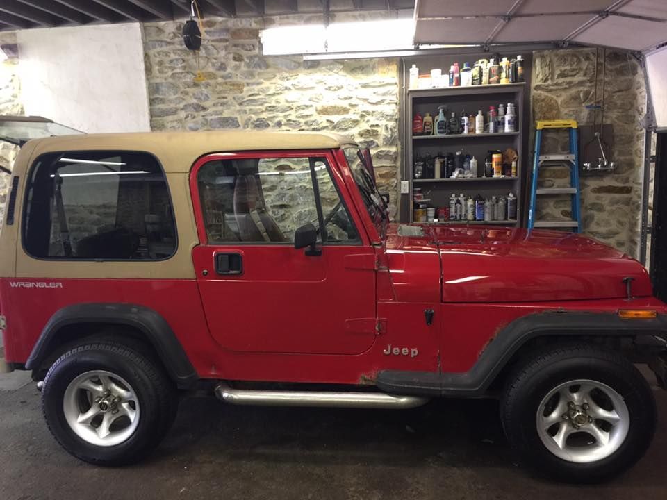 A red jeep with a tan top is parked in a garage