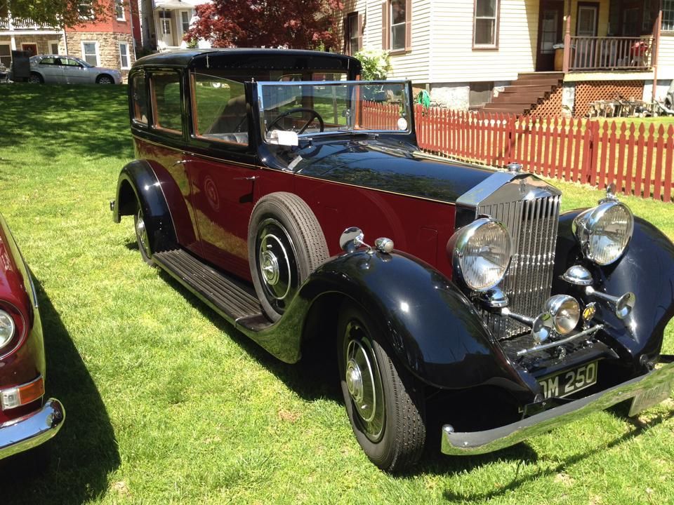 A red and black vintage car is parked in a grassy field.