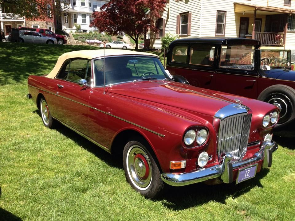 A red car with a white top is parked in the grass.
