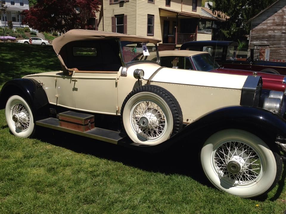 An old car with the top down is parked in the grass