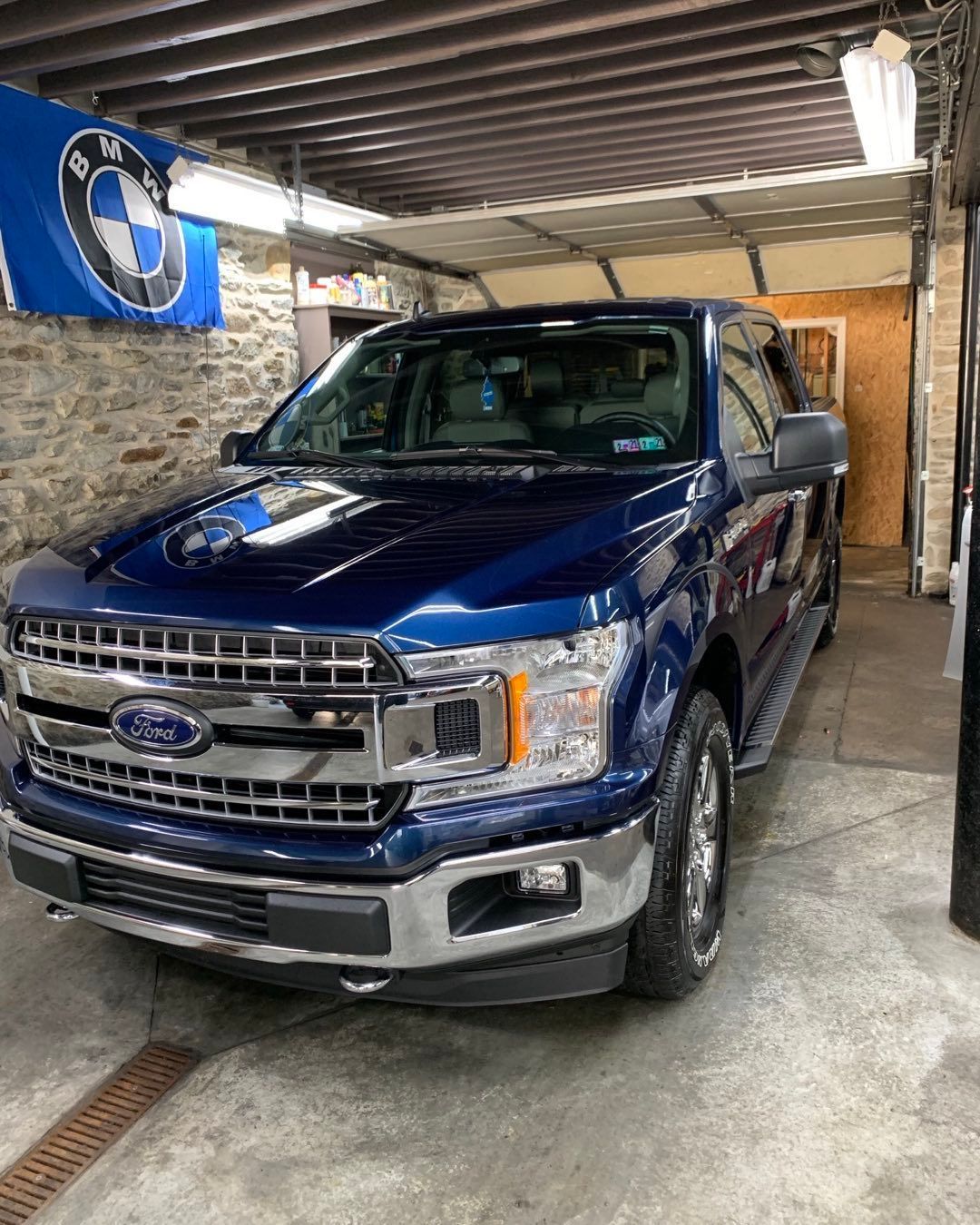A blue ford f150 is parked in a garage next to a bmw flag.