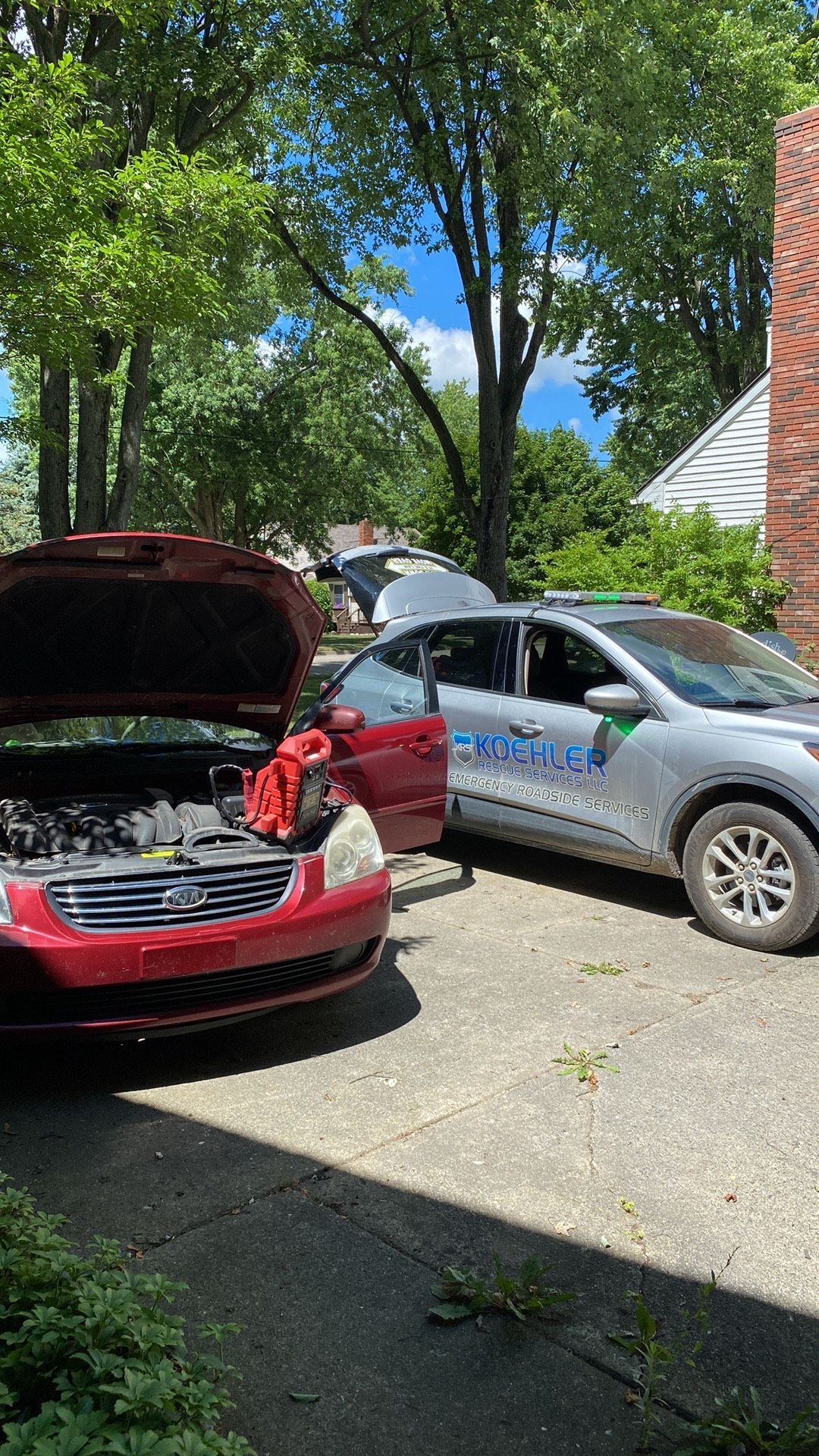 A red car is parked next to a silver car with its hood open.