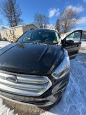 A black ford escape is parked in the snow with its doors open.