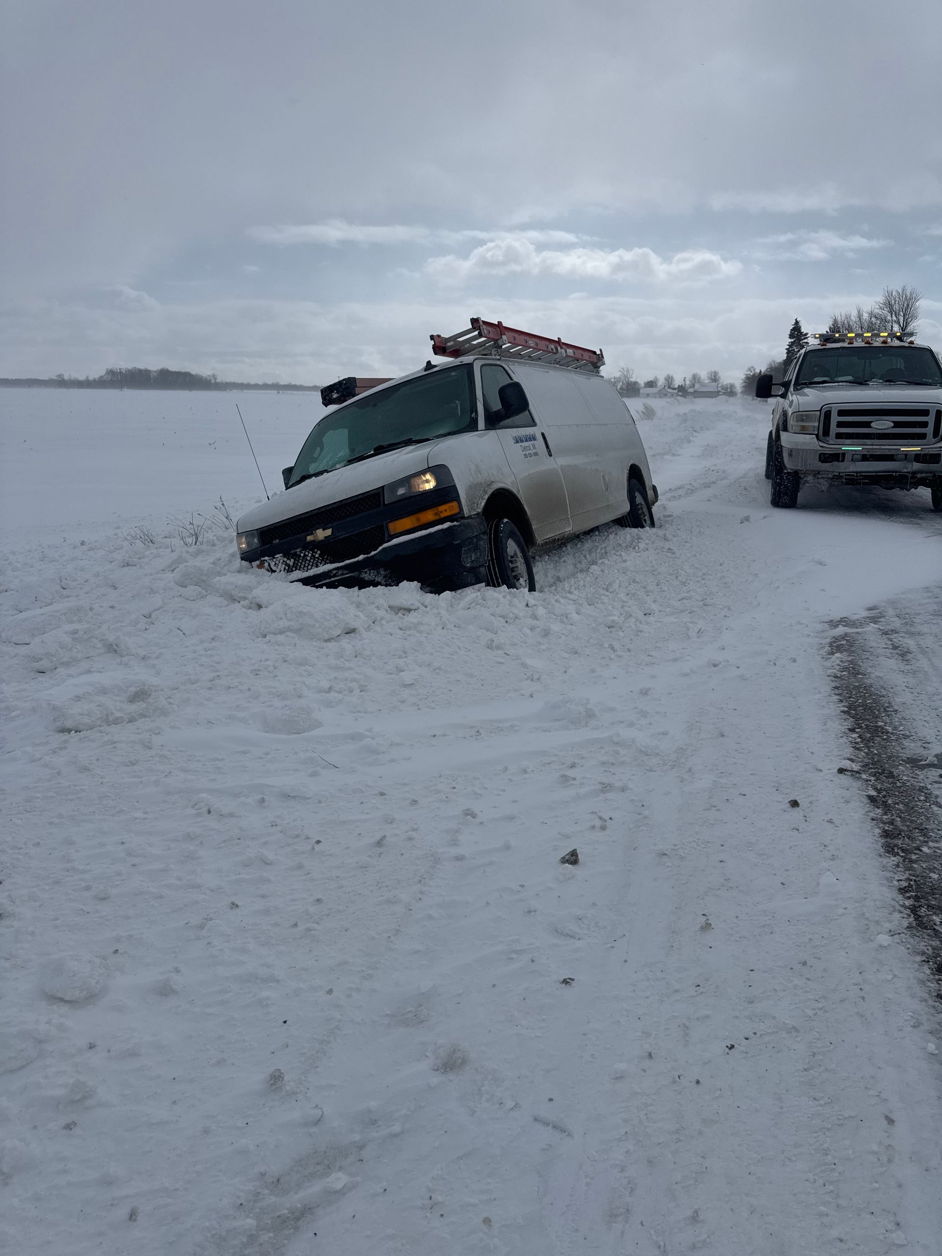 A white van is stuck in the snow on the side of the road.
