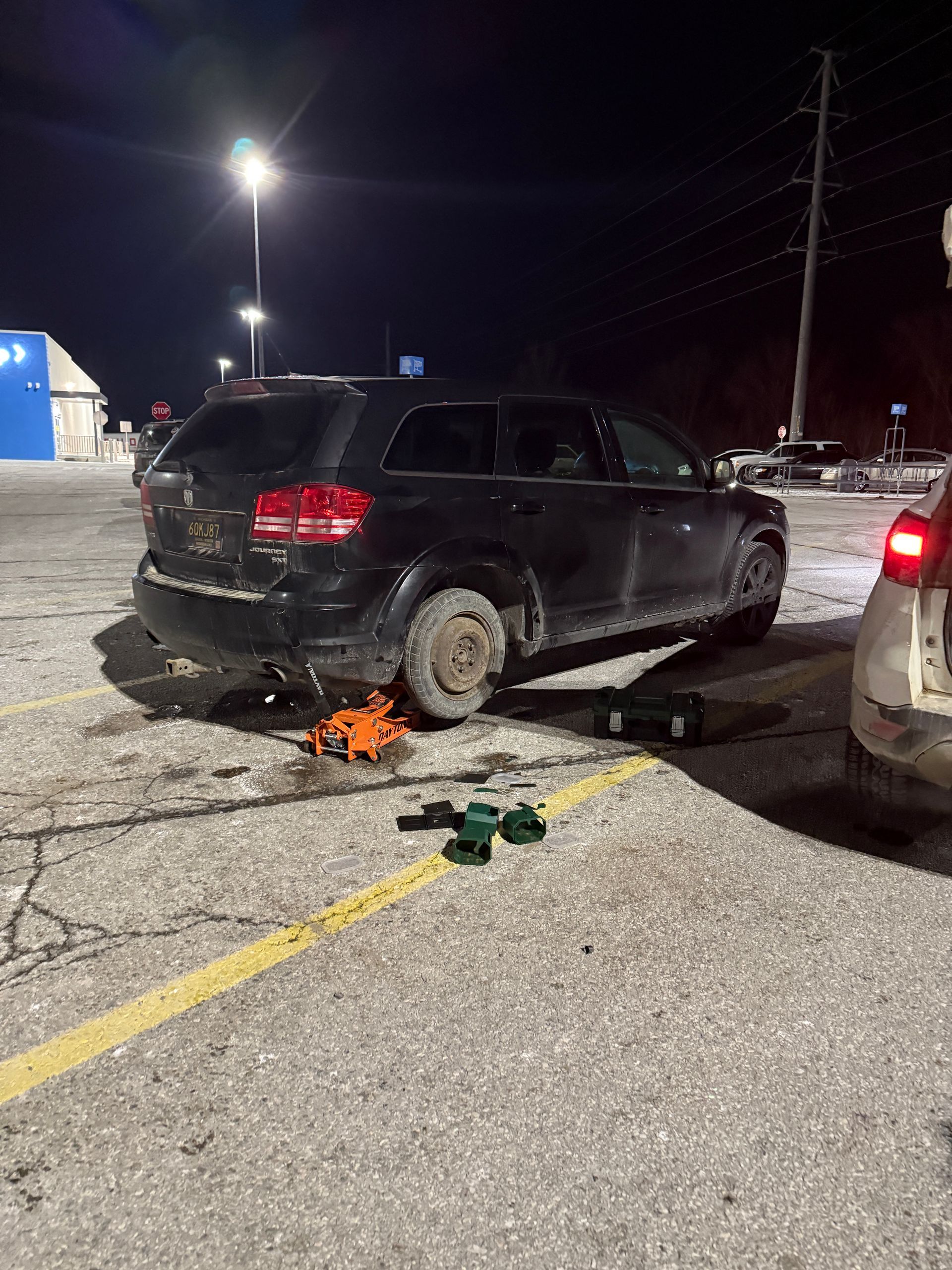 A car is sitting on a jack in a parking lot at night.