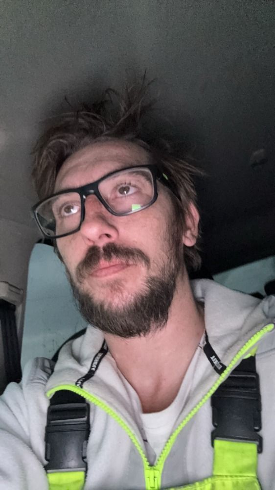 A man with a beard and glasses is sitting in a car.