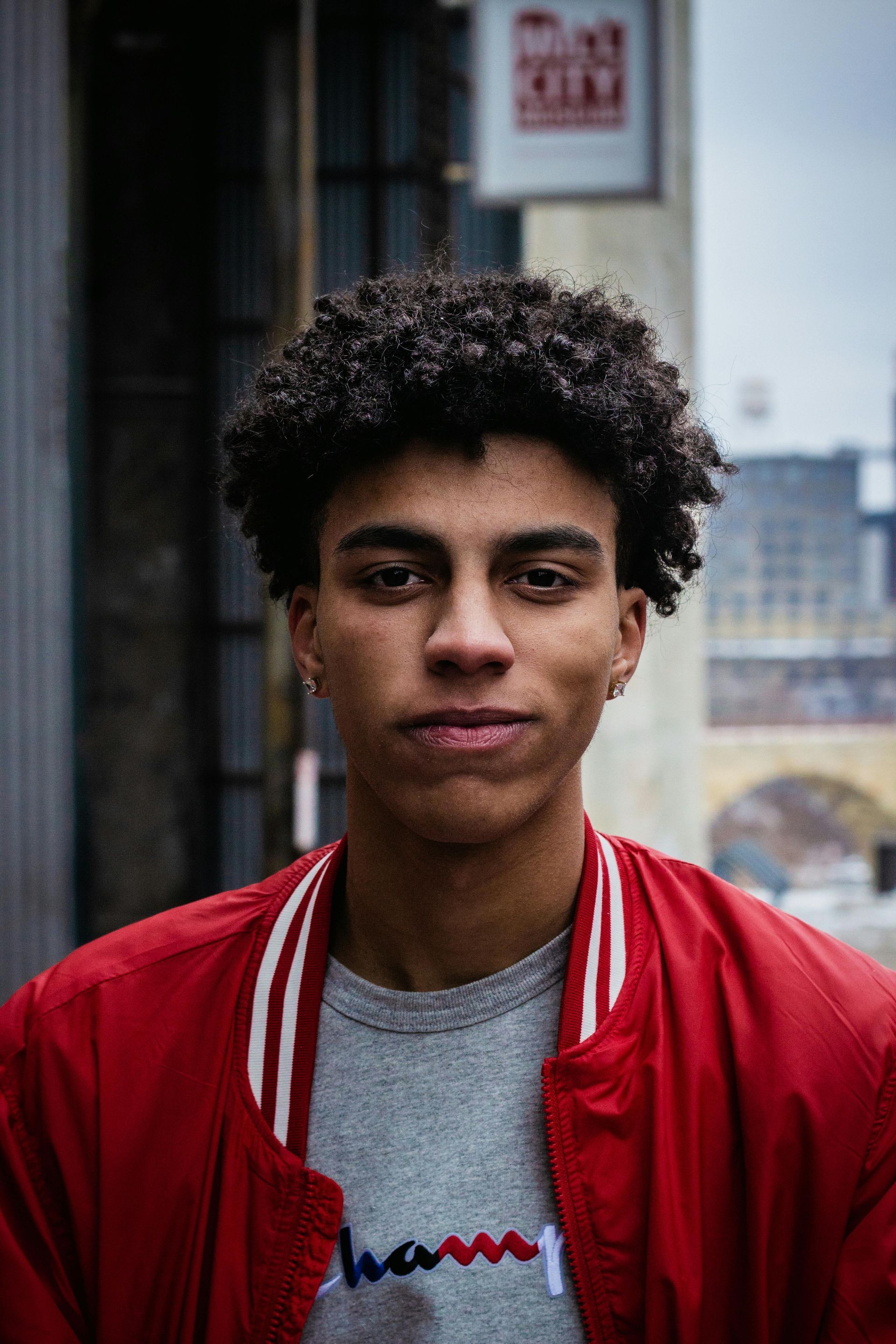 A young man with curly hair is wearing a red jacket and a gray t-shirt.