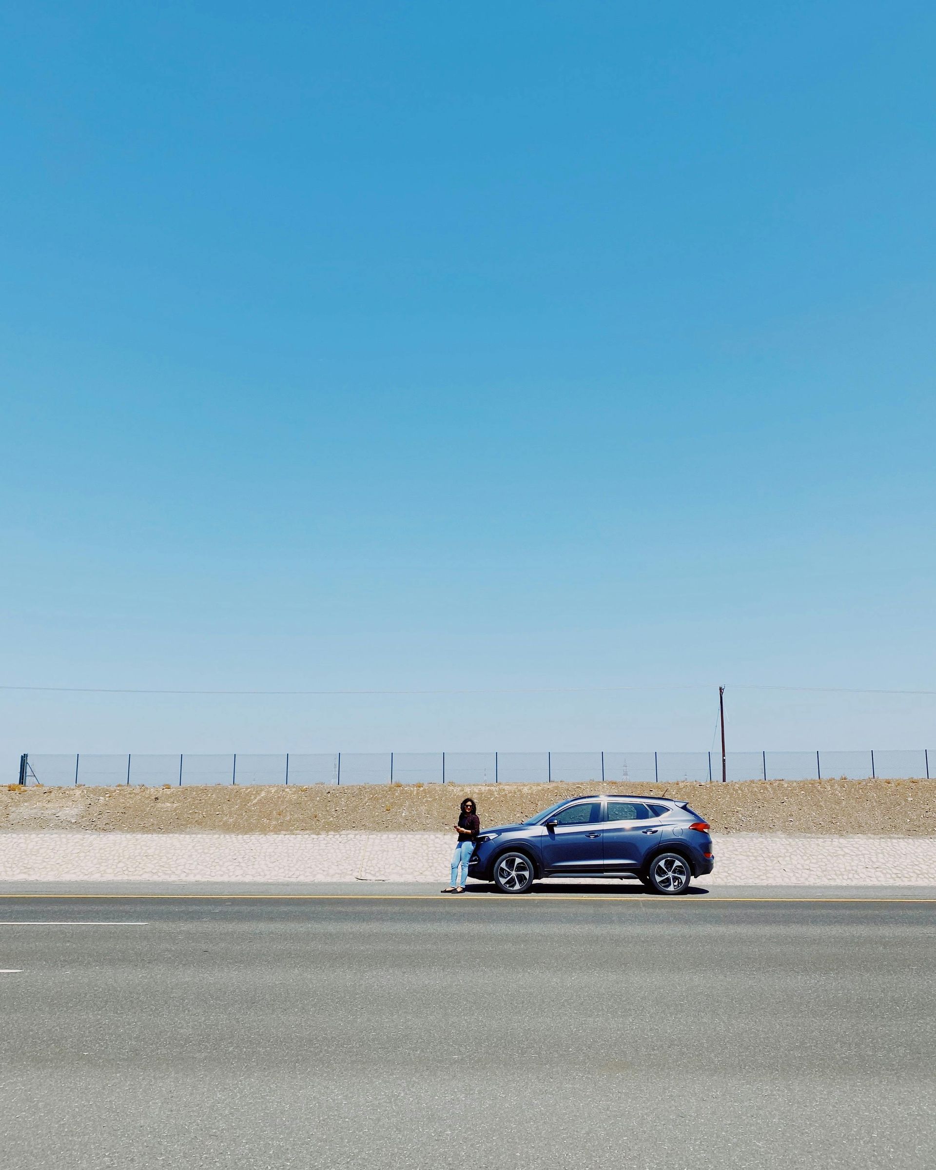A blue car is parked on the side of the road in the desert.
