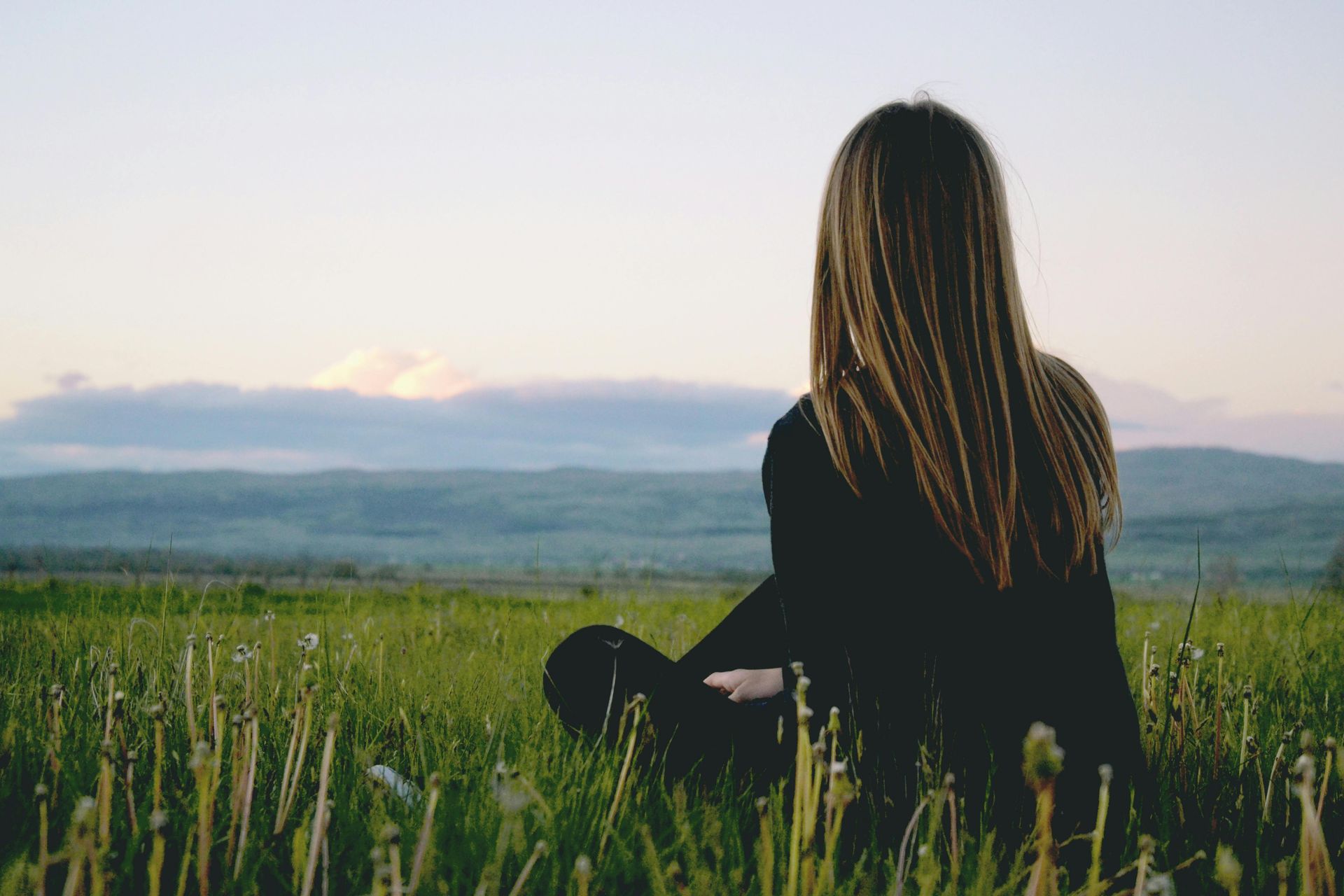 A woman is sitting in the grass looking at the mountains.