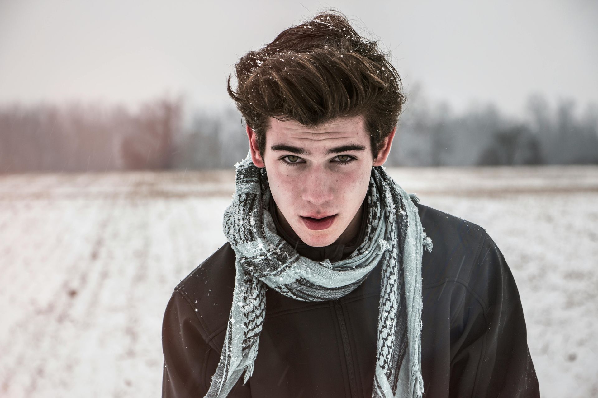A young man wearing a scarf and a sweater is standing in the snow.