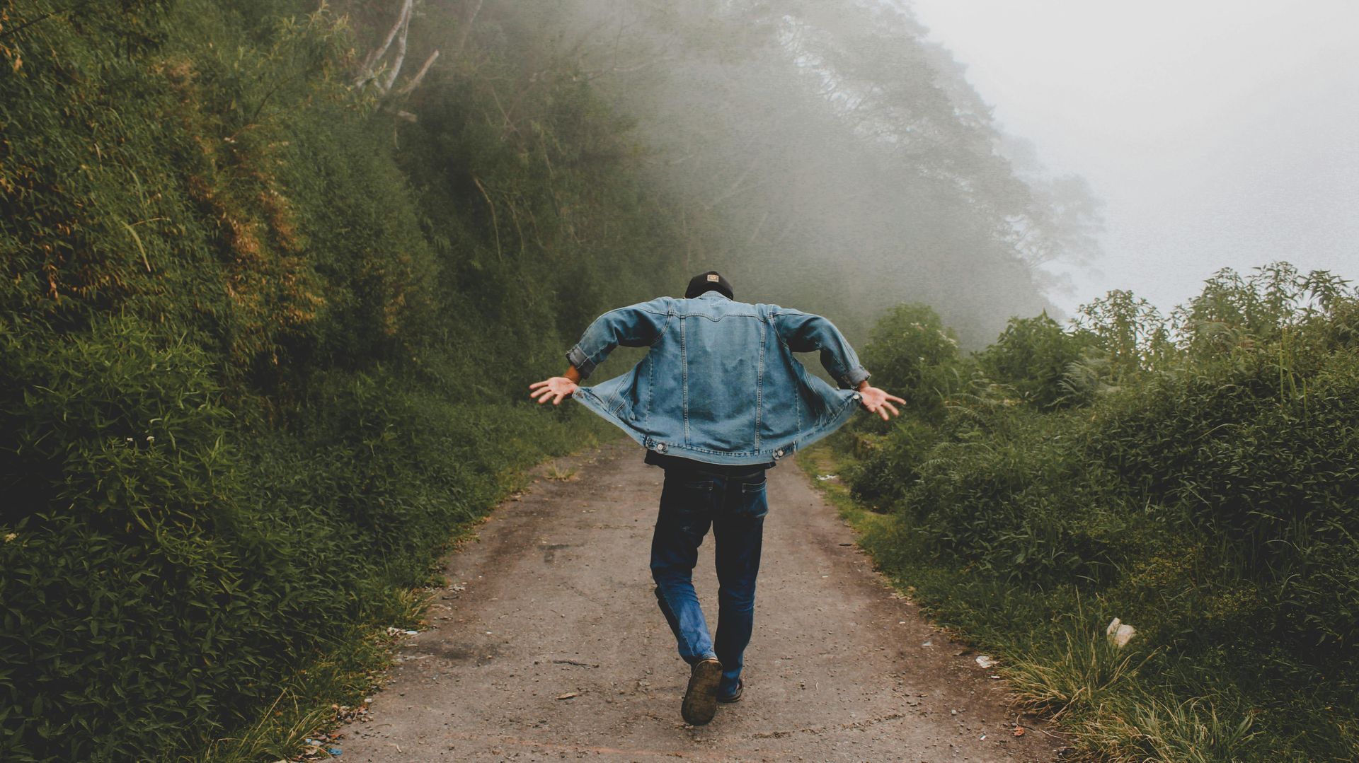 A man is walking down a dirt road with his arms outstretched.