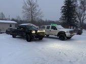 Two trucks are parked in the snow in front of a house.