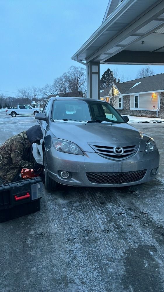A man is working on a car in the snow.