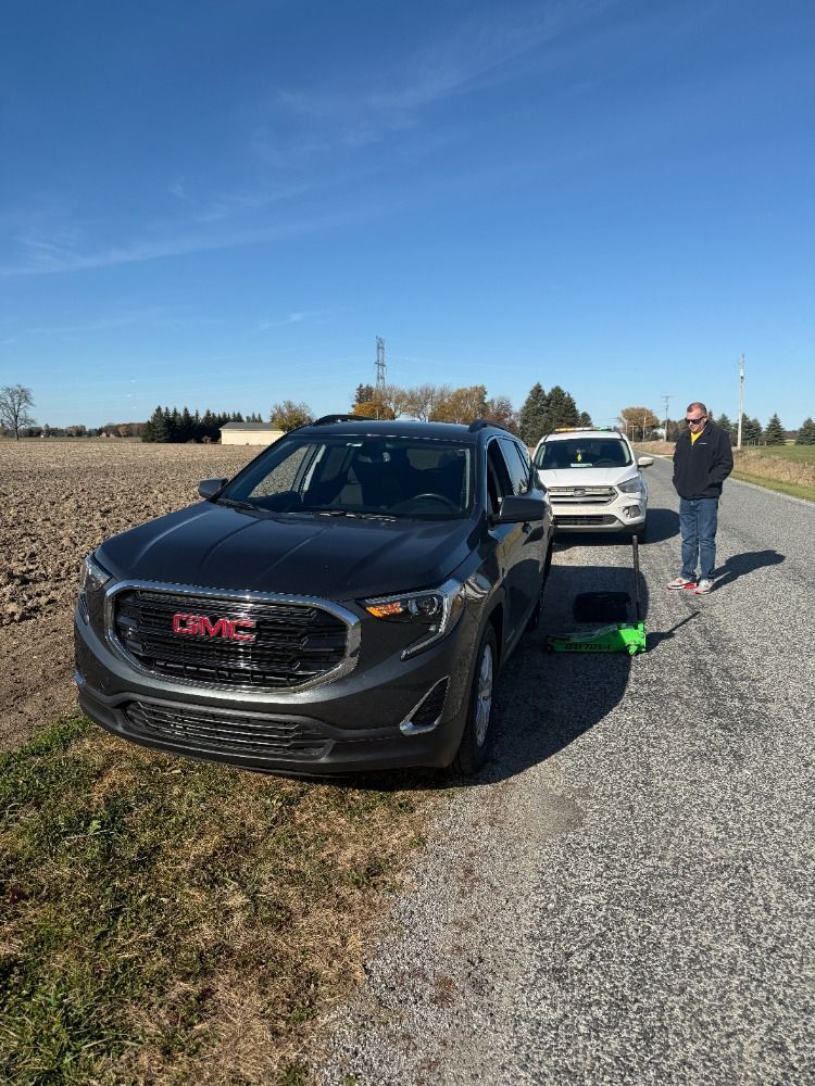A man is standing next to a gmc car on the side of the road.