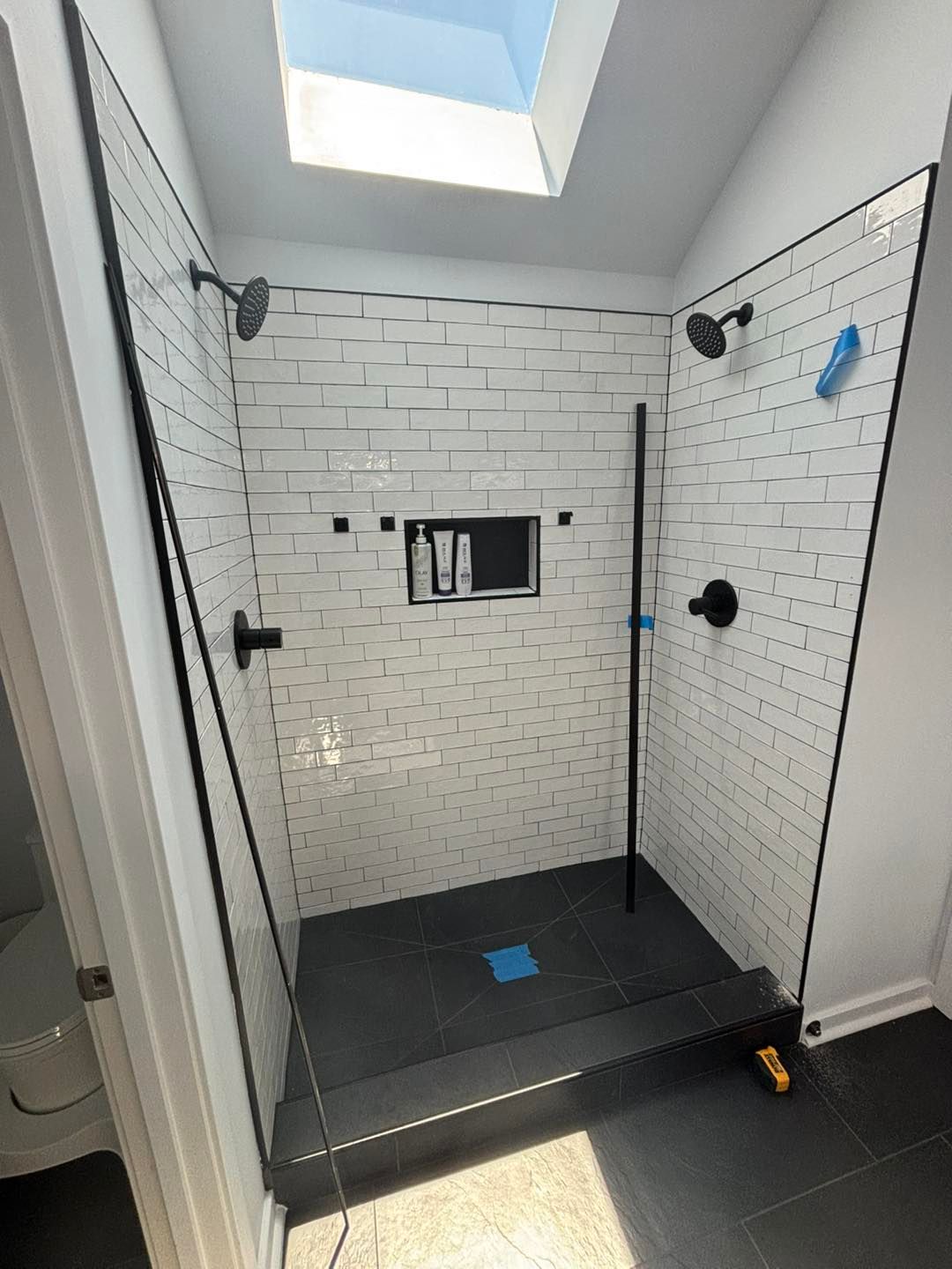Shower with black fixtures and gray tile, skylight overhead.