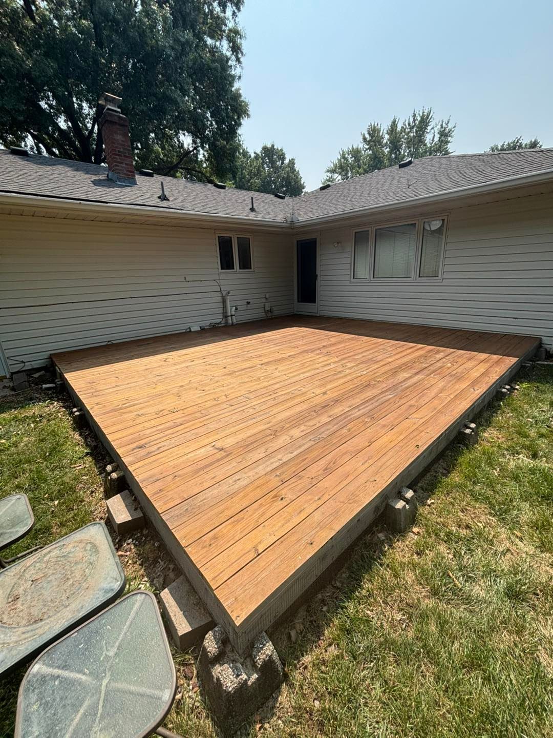 Wooden deck, built in a triangular shape, attached to a house with a green lawn.