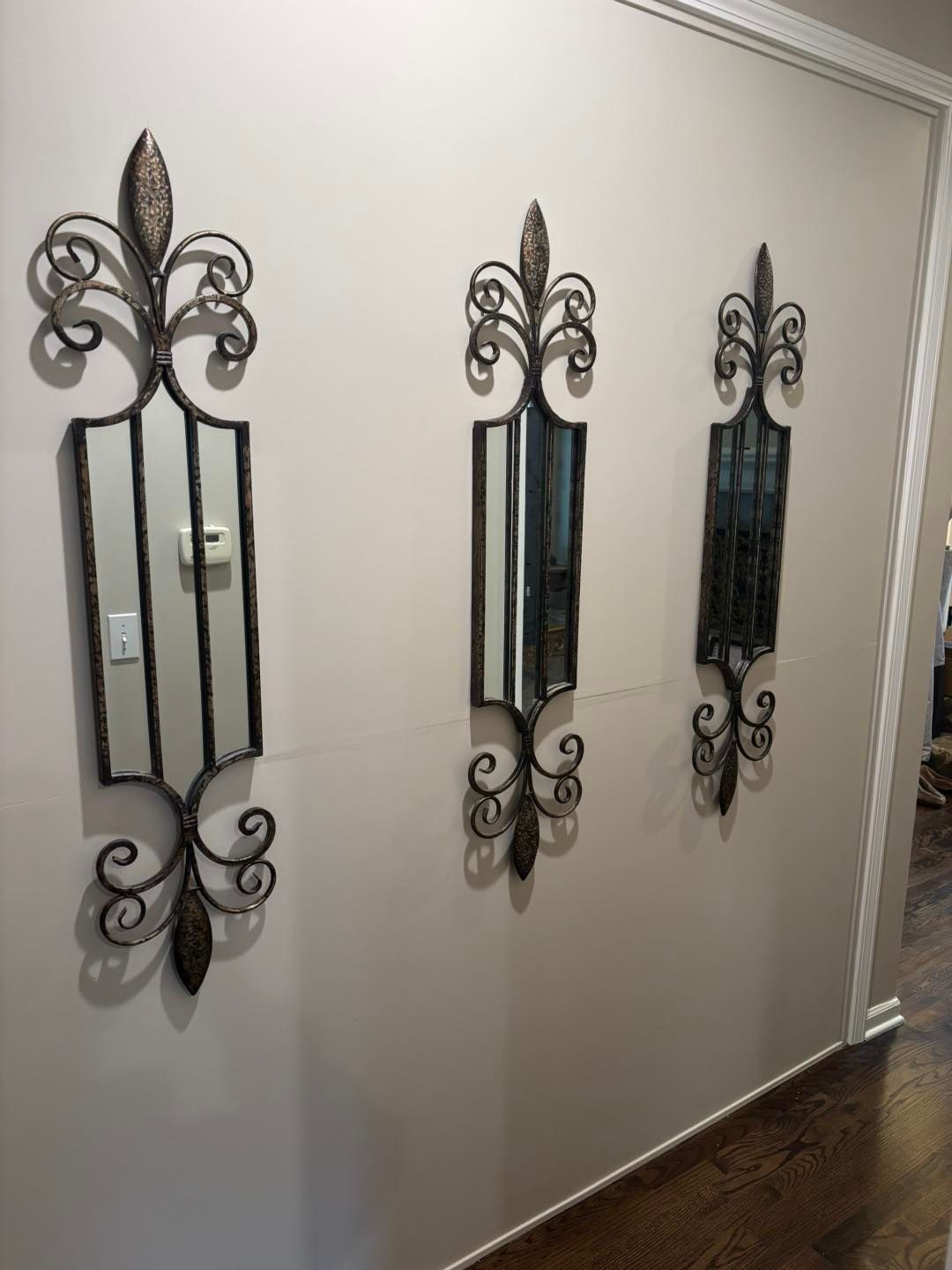 Three ornate metal-framed mirrors of varying designs hang on a neutral-colored wall in a hallway.