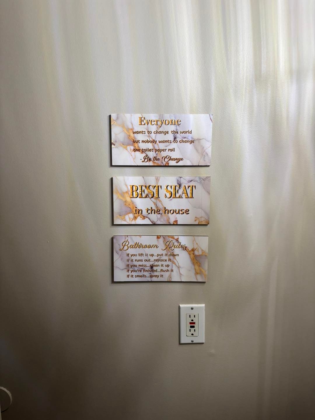 Three marble-patterned signs with gold lettering on a wall. The signs read