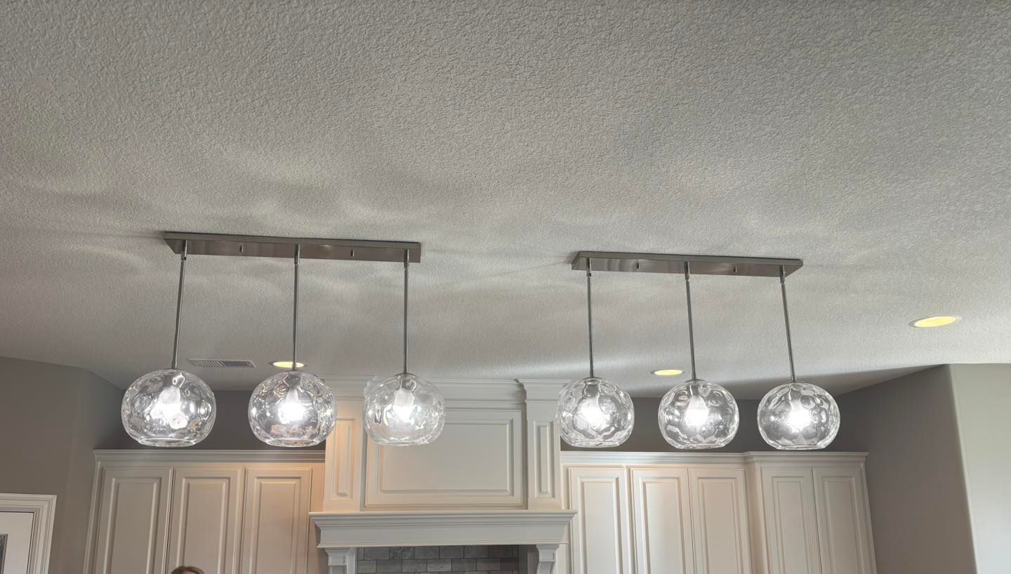 Two sets of three globe pendant lights above white kitchen cabinets, set against a textured ceiling.