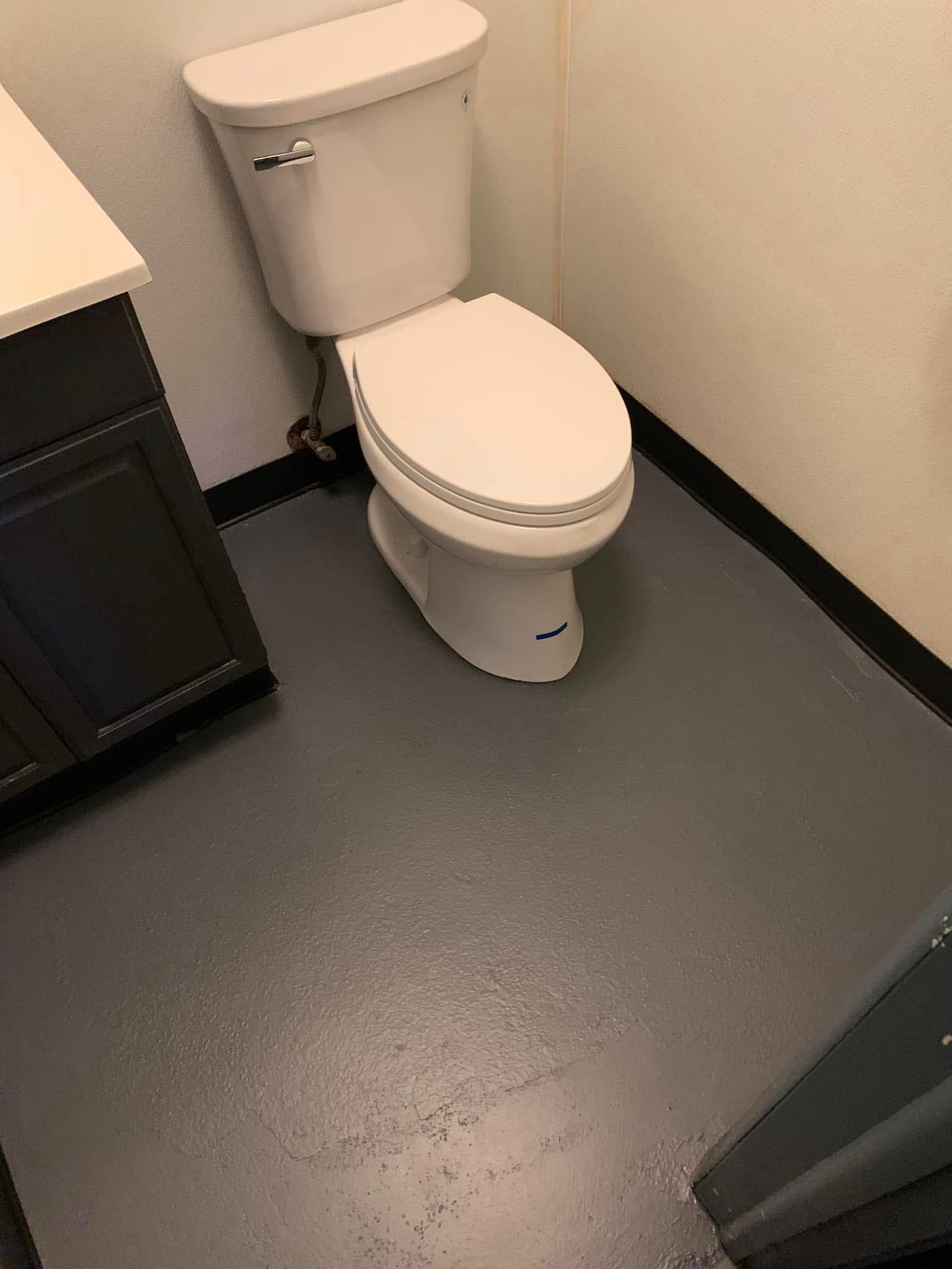 A white toilet in a small bathroom with dark gray flooring and a black vanity.