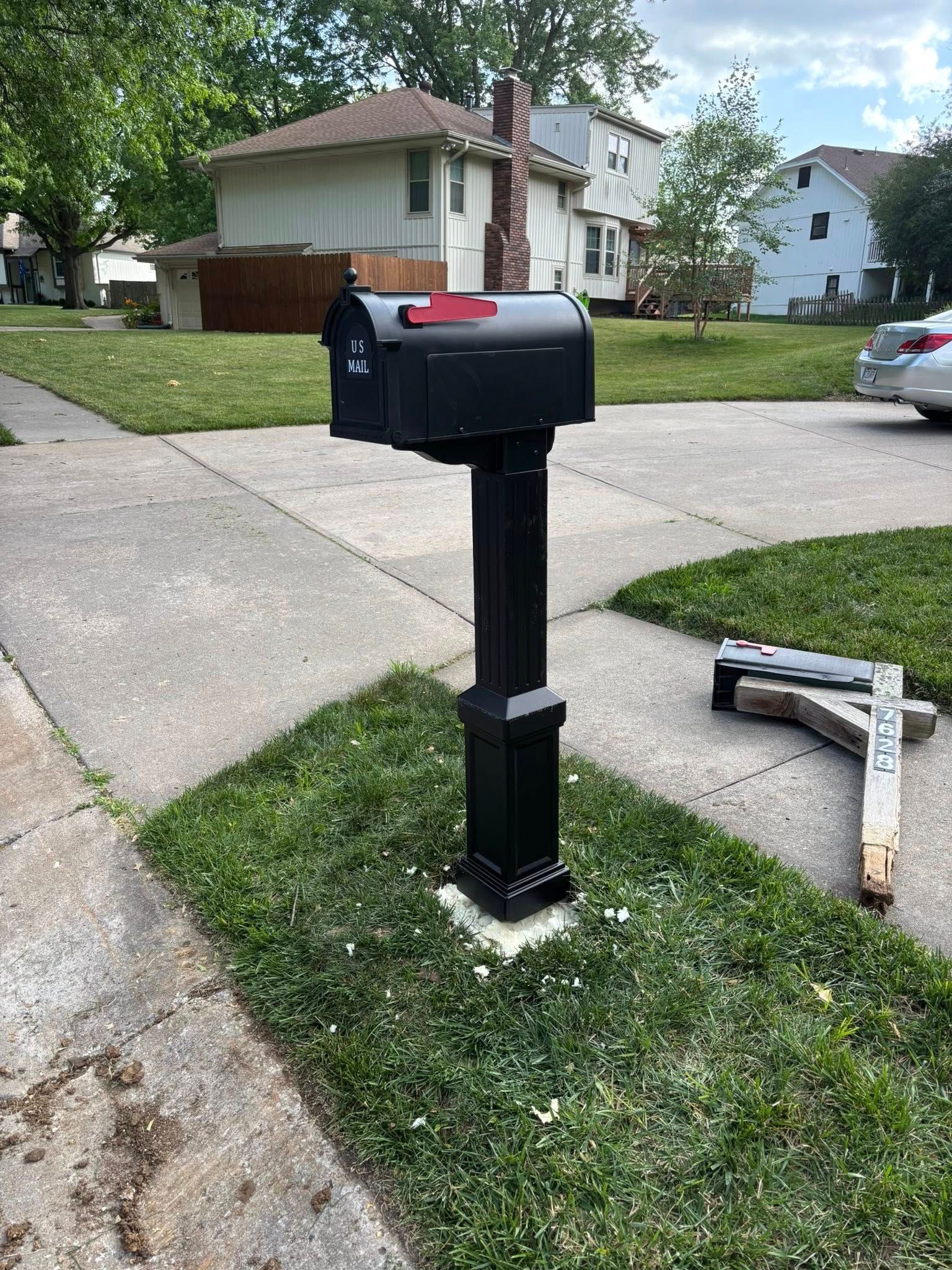 Black mailbox on a black post in a grassy area next to a sidewalk.