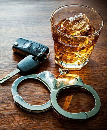 A pair of handcuffs , a car key , and a glass of whiskey on a wooden table.